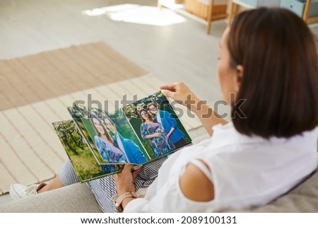 Woman looking at beautiful pregnancy photoshoot in family album. Mother looking at romantic maternity photo shoot of her pregnant daughter together with husband in good quality hardcover photo book