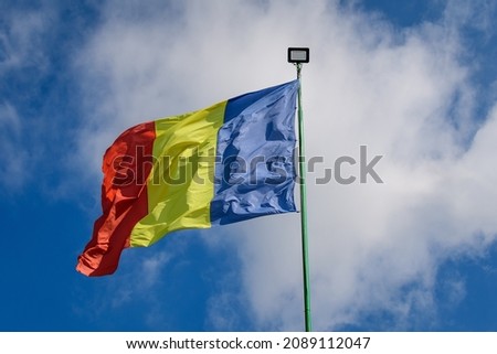 The Romanian national flags blowing in the wind in direct sunlight towards cloudy blue sky in a sunny spring day