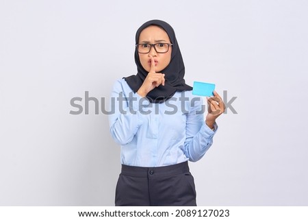 Portrait of pretty young Asian woman holds a credit card and makes silent gesture isolated on white background