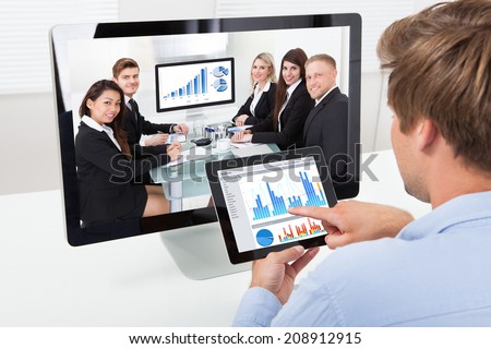 Rear view of businessman analyzing graphs on computer while video conferencing in office