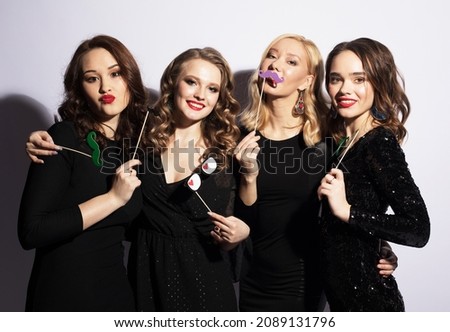 Beautiful young women in black cocktail dresses with party props, fake glasses and mustache