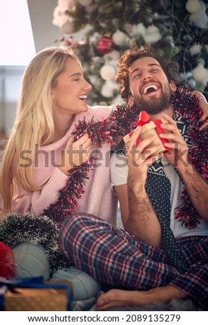 A guy can not hide her excitement because of a christmas present he got from his girlfriend while they are sitting on the floor during christmas holidays in a pleasant atmosphere at home together. 
