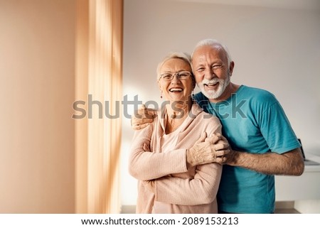 Senior couple hugging in a nursing home. A happy senior couple standing next to a window in a nursing home, hugging and smiling. They have all care they need. Royalty-Free Stock Photo #2089153213