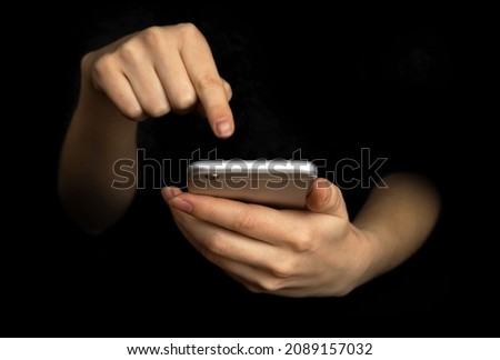 Person uses mobile phone with index finger. Hand with modern smartphone on a black background, communication and techonology concept