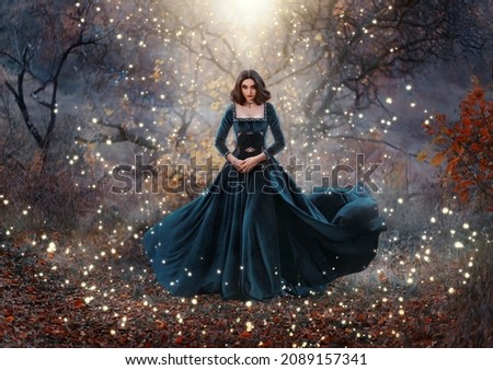 Gothic fantasy woman witch holding magic book hands. Long black velvet medieval vintage dress flies wind. Girl conjures. Bright divine light glow sparkles magic circle around lady. Autumn forest tree Royalty-Free Stock Photo #2089157341