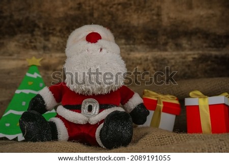 Santa claus doll on burlap on a christmas tree background and two gift boxes