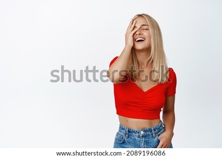 Attactive blond woman in stylish summer outfit, laughing and touching her face, smiling carefree, standing over white background
