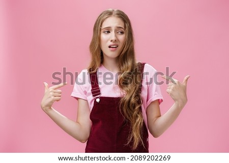 Self-assured arrogant young female student with high ego standing cocky and brag about herself pointing at her with cool snobbish look looking away to right with contempt posing over pink wall Royalty-Free Stock Photo #2089202269