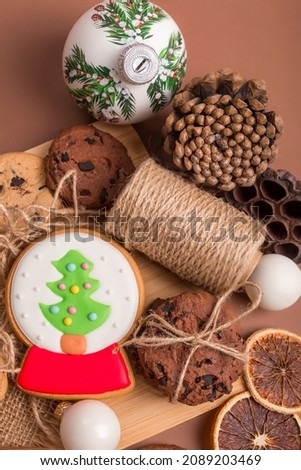 Beautiful Christmas and New Year composition with ginger bread and chocolate cookies, christmas white toys, chinnamon sticks, cane candies and orange slices on wooden desk on brown background. 