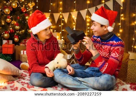 Portrait of a boy and a girl in New Year decoration. They play and take photos. Festive lights, gifts and a Christmas tree decorated with toys.