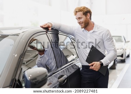 Man minded customer male buyer client in white shirt hold clipboard papers document lean on car choose auto want buy new automobile in showroom vehicle dealership store motor show indoor Sales concept