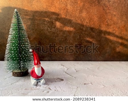 mini santa claus mock skiing board on large imitate snow field with demo white flake green christmas tree behind with warm light blurred shadow effect earth tone background color and contrast lighting