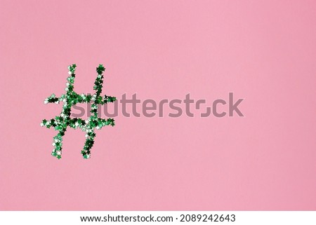 green shiny hashtag on a light pink background. Online technology concept and social media marketing. Space for text and notes, copy, top view, flat lay.
