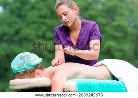 Beautiful professional massagist. Woman is relaxing on massage table masseur doing massage with fists massaging female back in spa salon outdoors. Natural background. Spa treatment, health, body care Royalty-Free Stock Photo #2089245673