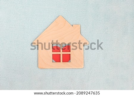Wooden house symbol on light blue fabric textured background. A red heart is visible in the window of the house. Selective focus.
