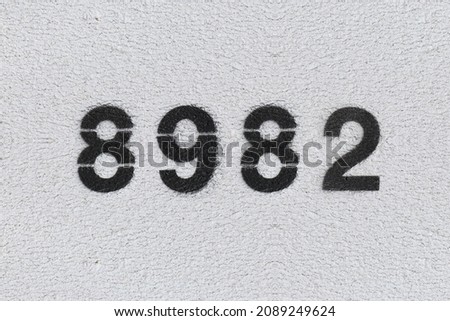 Black Number 8982 on the white wall. Spray paint. Number eight thousand nine hundred and eighty two.
