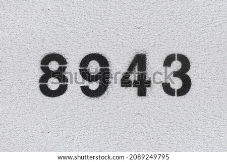 Black Number 8943 on the white wall. Spray paint. Number eight thousand nine hundred forty three.