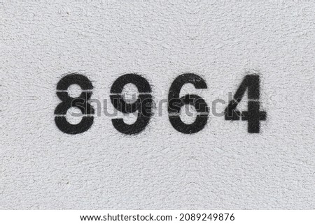 Black Number 8964 on the white wall. Spray paint. Number eight thousand nine hundred and sixty four.
