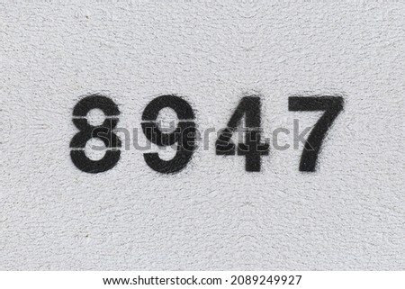 Black Number 8947 on the white wall. Spray paint. Number eight thousand nine hundred forty seven.
