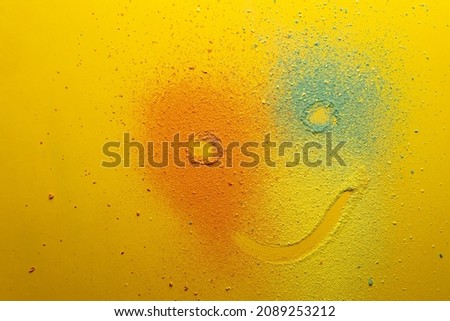 Cute emoticon that looks like a clown is drawn on a multicolored powder, on a bright background. Holiday concept. Copy space. 
