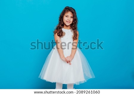 a little curly girl in a white princess dress on a blue background
