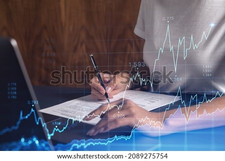 A client in casual wear is signing the contract to invest money in stock market. Internet trading and wealth management. Forex and financial hologram chart over the desk. Women in business concept.