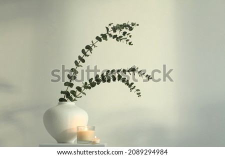 Green leaf eucalyptus bouquet in white bowl and burning candle on gray interior. Selective soft focus. Minimalist still life. Light and shadow nature horizontal background.