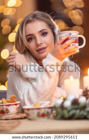 Young beautiful woman in a Christmas atmosphere holding a cup with coffee or tea.