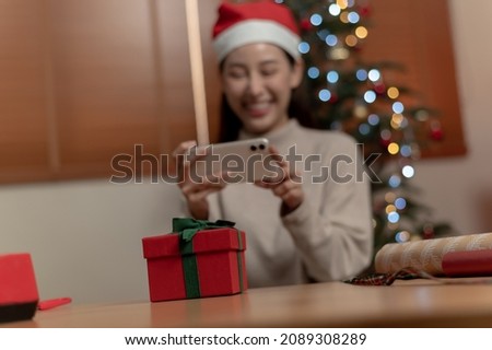 Selective focus on Christmas gift box, Asian woman using smartphone taking photo of new year Christmas present box before send or received from friend or family during Christmas festival celebration.