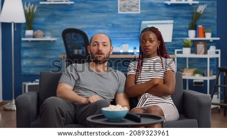 POV of interracial couple being shocked watching television and drama movie at home. Multi ethnic husband and wife looking at camera while sitting on couch in living room. Mixed race people Royalty-Free Stock Photo #2089323961