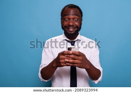 Portrait of businessman holding mobile phone playing exciting new action game looking down at the screen. Happy person enjoying overwhelming gadget app having fun in office break.