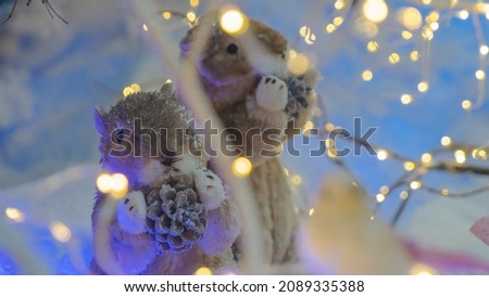 Two toys funny rodent are standing under a tree. Defocused foreground with lights. Decorations for the shopping center and shop windows. Xmas concepts.