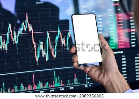 Male cryptocurrency trader investor analyst hand holding cell phone with white mockup screen doing stock market data price charts analysis using cryptocurrency trading mobile app, stock application.