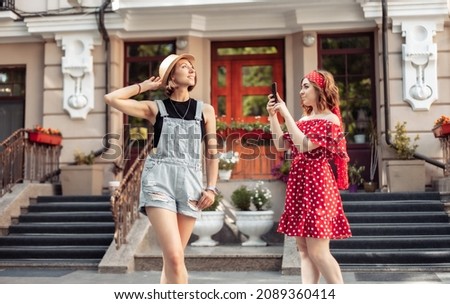 Young woman photographs her girl friend on the phone in the city. Has a fun 