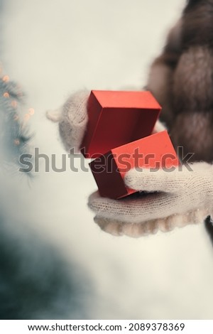 Female hands hold red christmas present in white mittens