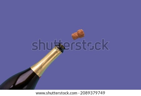 A bottle of champagne and a cork are open on a very peri lilac background.