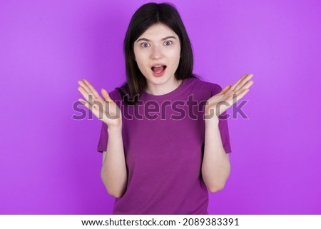 Surprised terrified Caucasian woman wearing purple T-shirt isolated over studio background Gestures with uncertainty, stares at camera, puzzled as doesn't know answer on tricky question, People, body 