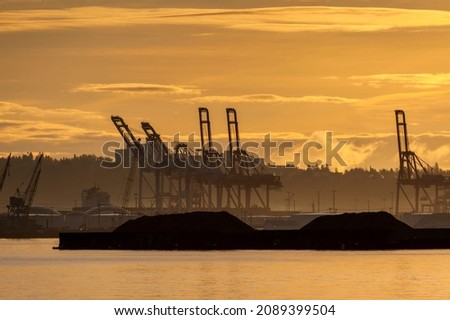 Sunrise on Elliott Bay with Silhouetted Seattle Dockyard Cranes. Waterfront with cranes for loading shipping containers onto container ships. Royalty-Free Stock Photo #2089399504