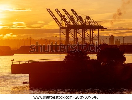 Sunrise on Elliott Bay with Silhouetted Seattle Dockyard Cranes. Waterfront with cranes for loading shipping containers onto container ships. Royalty-Free Stock Photo #2089399546