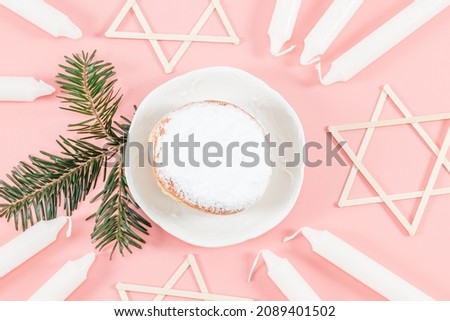 A donut with powder, nine white candles, a fir branch and wooden stars of David lie on a pink background, close-up top view. Hanukkah Celebration Concept.