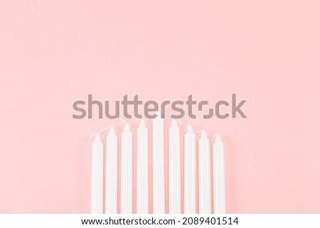 Nine white candles lie from the bottom in the middle on a pink background with a copy of the space on top, flat lay close-up. Hanukkah Celebration Concept.