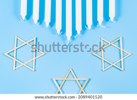 Nine white candles and three wooden David stars candles lie on a blue background with copy space in the center, flat lay close-up. Hanukkah Celebration Concept.