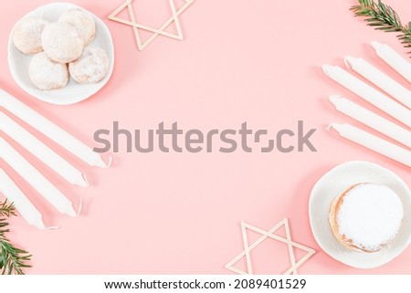 Donuts with powder in saucers, white candles, fir branches and wooden stars of David lie on the sides on a pink background with copy space in the center, top view close-up. Hanukkah Celebration Concep