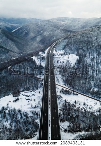 Amazing aerial view of a road. Stunning snow landscape with river and trees. Cars driving on the road. Snow drone shot. High quality photo