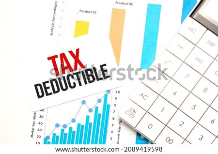 Office workplace table with calculator, graphs, reports and the text TAX DEDUCTIBLE on a small piece of paper on multicolored backgroundd.