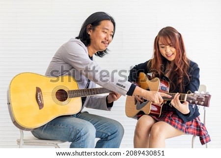Young Asian teenager is learning to play guitar by professional teacher who showing simple chords for music class school