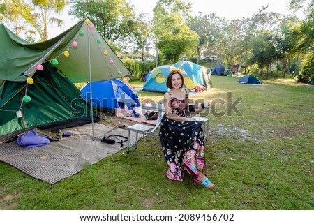 Go camping to see the winter nature in Thailand, under the trees with rivers and streams flowing through the morning, good weather, beautiful sunlight, taking a picture of a smiling Thai woman 
