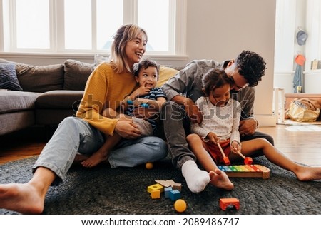 Young parents playing with their son and daughter in the living room. Mom and dad having fun with their children during playtime. Family of four spending some quality time together at home. Royalty-Free Stock Photo #2089486747