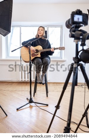 A young girl plays the guitar, recording video and sound.