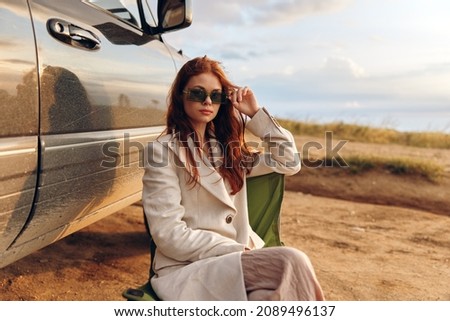 beautiful woman in a coat outdoors sitting on a chair near the car harvest